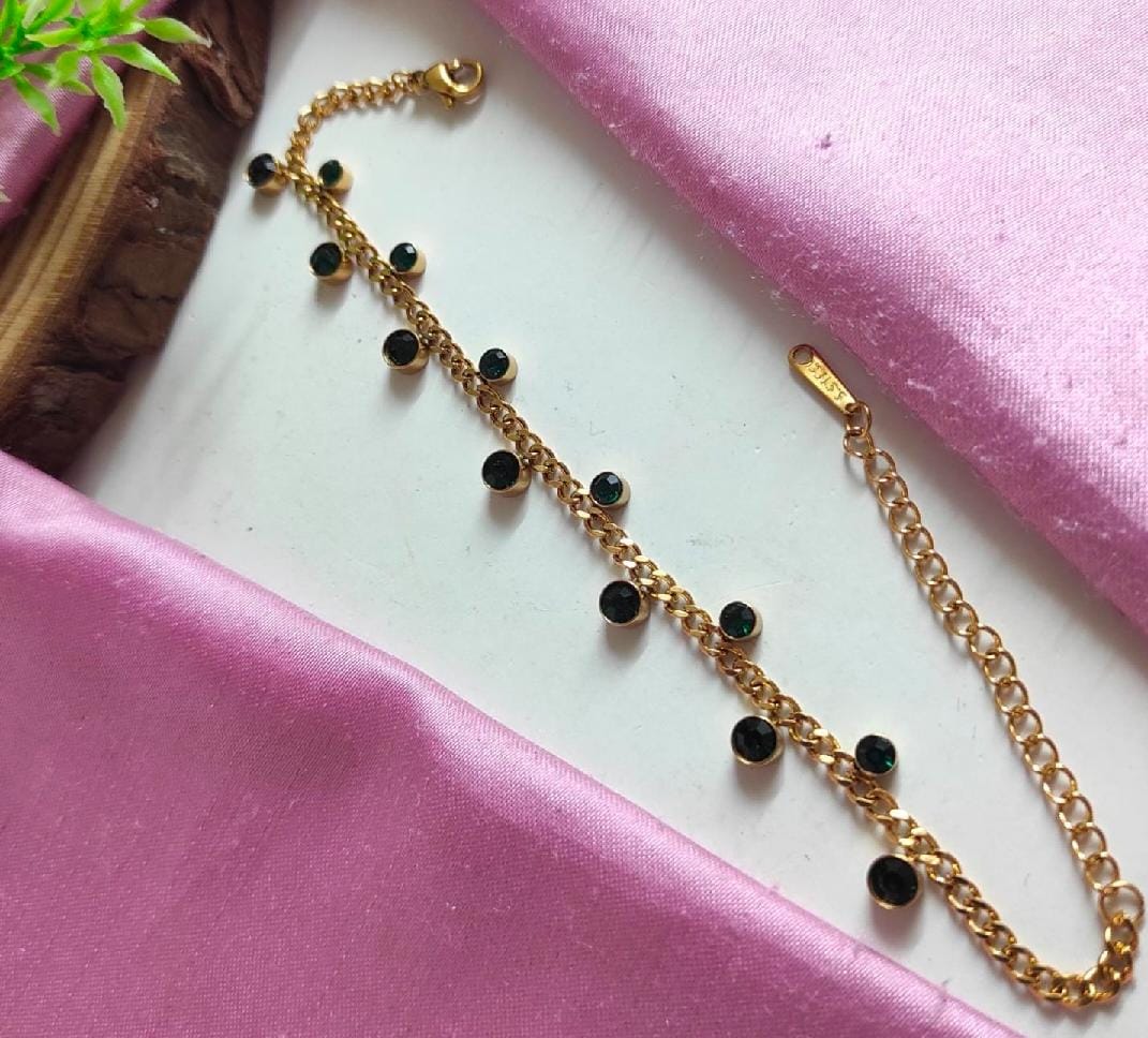 Gold anti tarnish bracelet with black beads on a pink fabric background